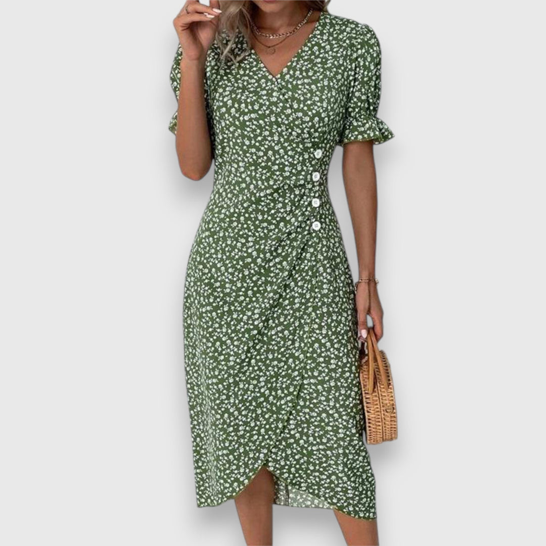 Green floral dress with ruffled sleeves and button details, woman carrying straw handbag, studio backdrop.