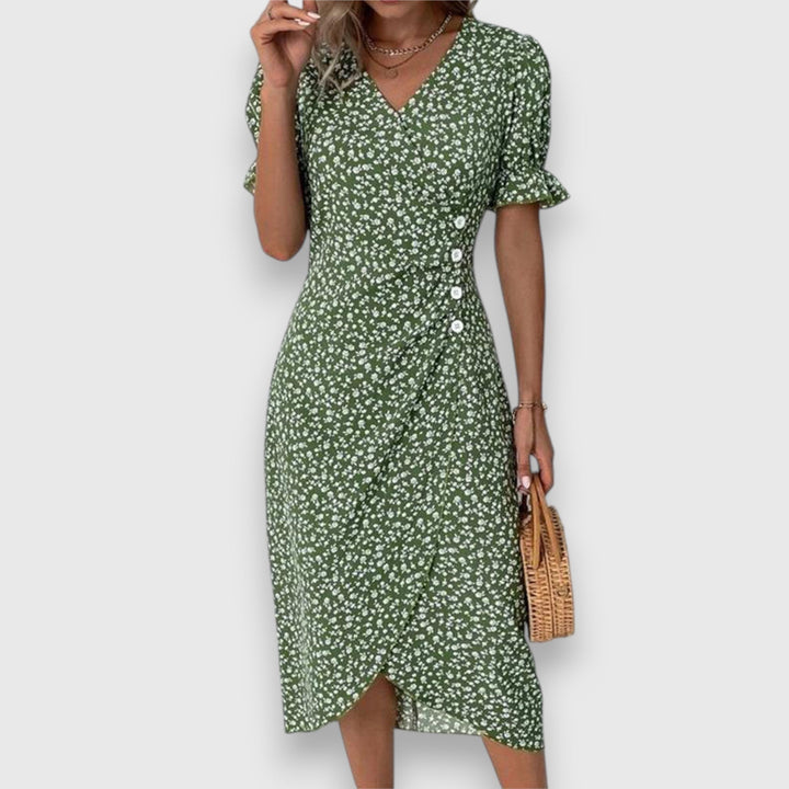 Green floral dress with ruffled sleeves and button details, woman carrying straw handbag, studio backdrop.