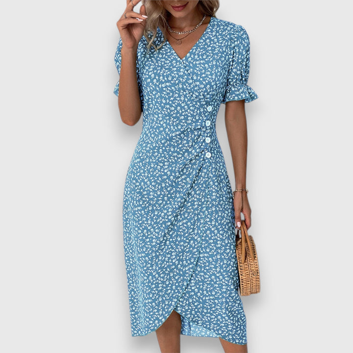 Blue floral dress with ruffled sleeves and button detail, woman holding straw handbag, studio backdrop.