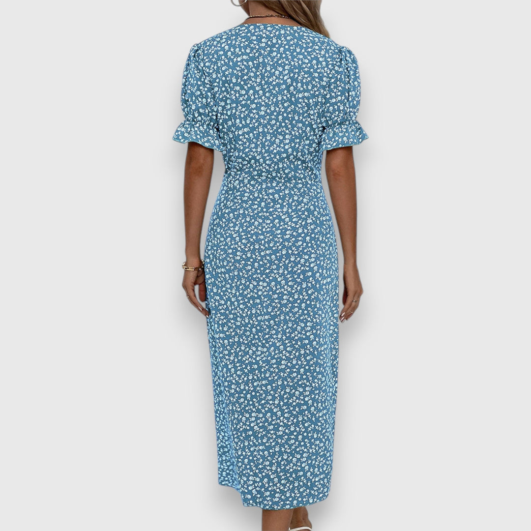 Back view of blue floral dress with gathered sleeves, woman standing, studio background.