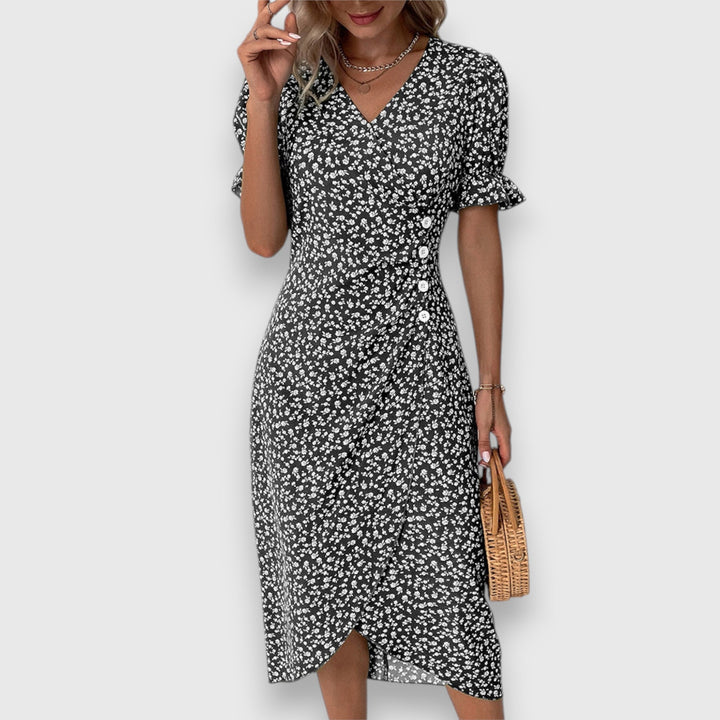 Black floral dress with ruffled sleeves and button accents, woman holding handbag, studio setting.