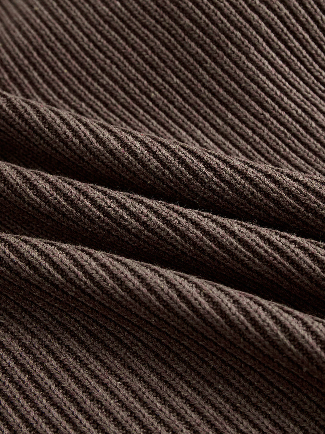 Close-up of dark brown ribbed sweater fabric, showcasing the detailed texture and cozy, soft appearance.