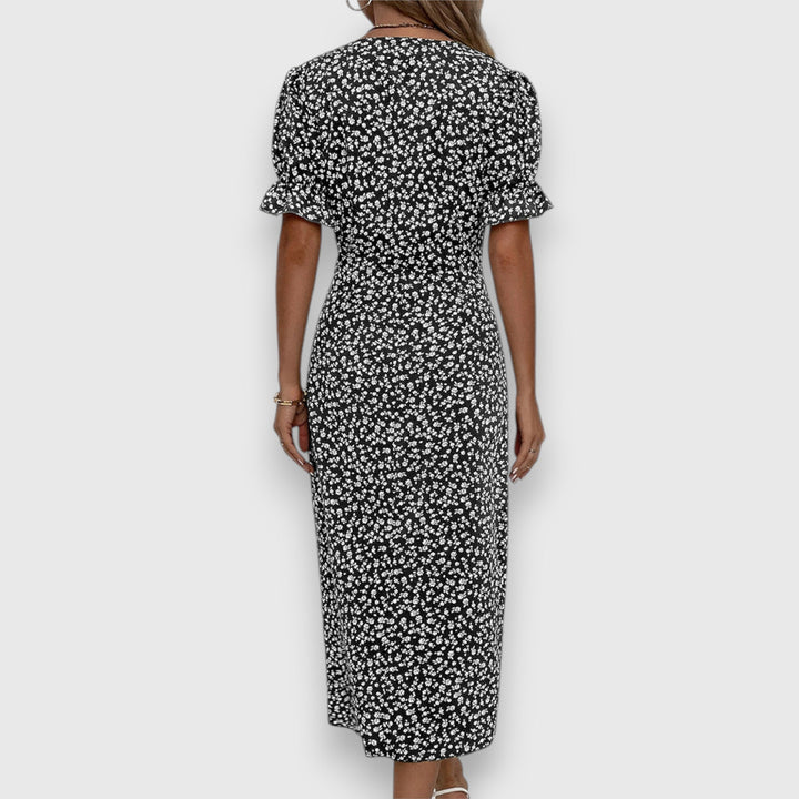 Back view of black floral dress with ruched sleeves, woman standing, studio background.