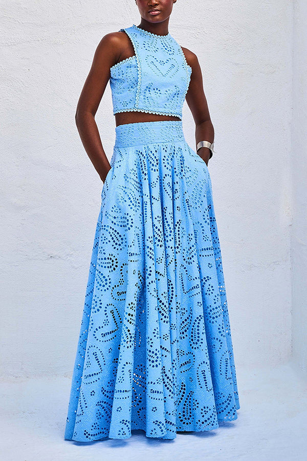 Woman in a blue embroidered skirt and top set standing against a white wall in a bright setting.