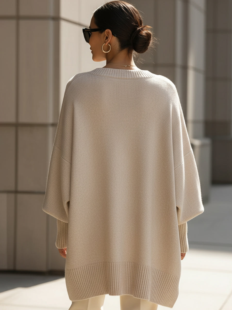Back view of a woman wearing a beige oversized sweater, paired with white pants, in an urban setting.