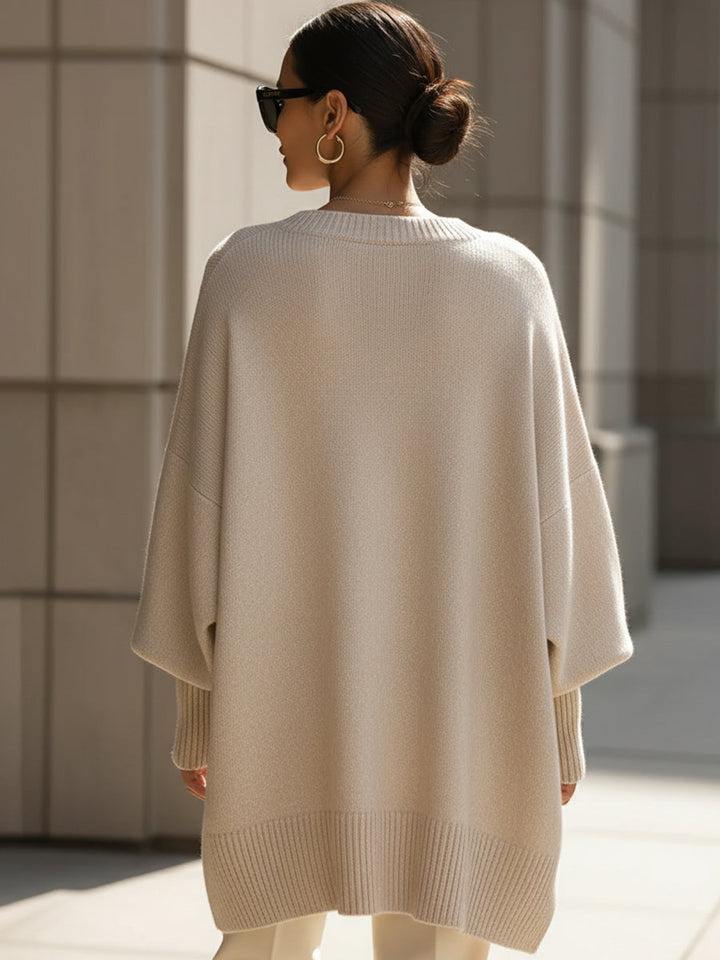 Back view of a woman wearing a beige oversized sweater, paired with white pants, in an urban setting.