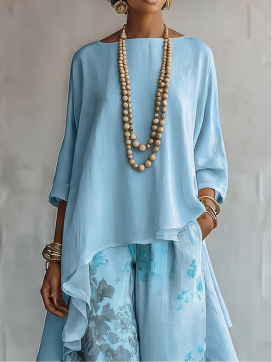 Close-up of light blue top with flowing design, paired with patterned pants, in studio.