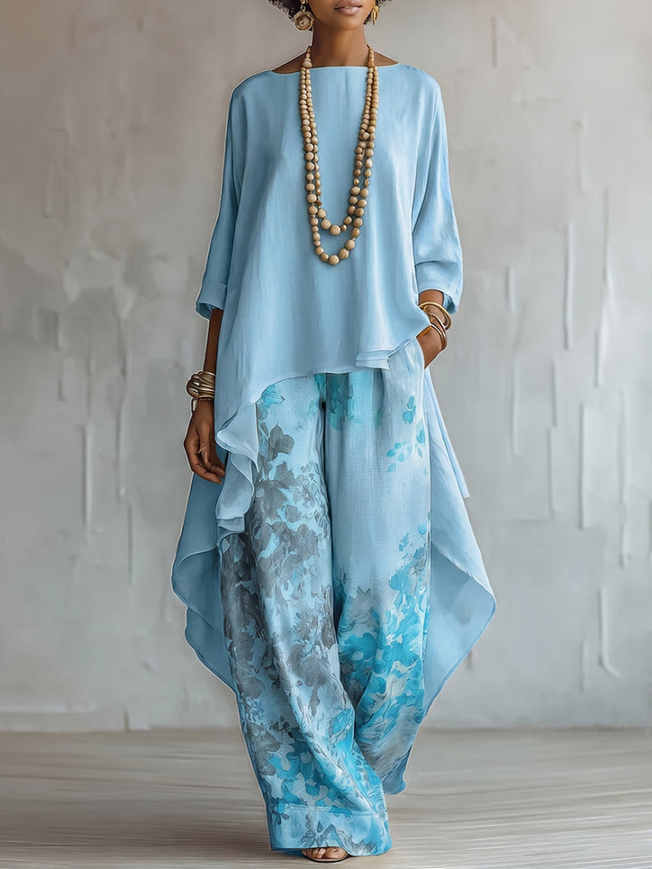 Model wearing light blue flowing set with floral pants and layered top, in a textured studio setting.