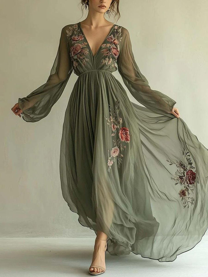Elegant chiffon dress in olive green with floral embroidery, long flowing sleeves, and a pleated skirt, worn indoors.