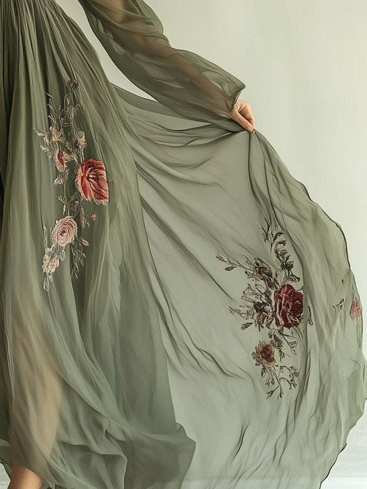 Detailed view of dress fabric in olive green with red floral embroidery and flowing texture, displayed indoors.