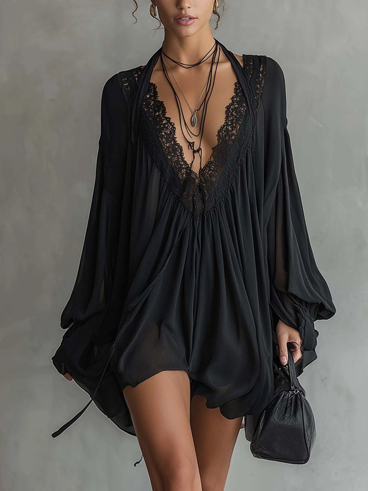 Black mini dress with lace neckline and flowing sleeves, accessorized with layered necklaces, held against a gray studio background.