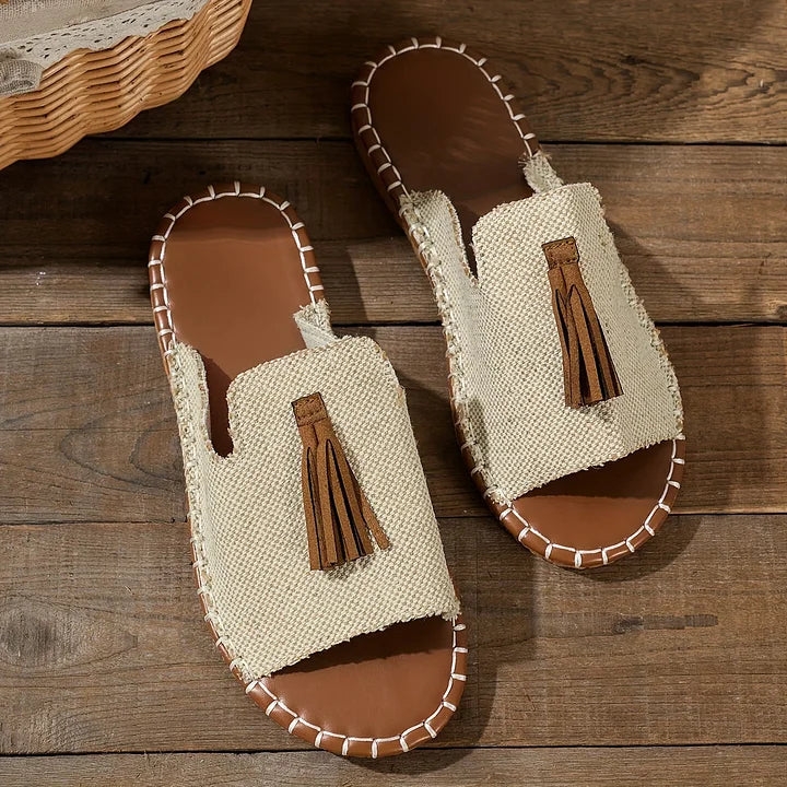 A pair of beige orthopedic sandals with tassels on wooden floor indoors.