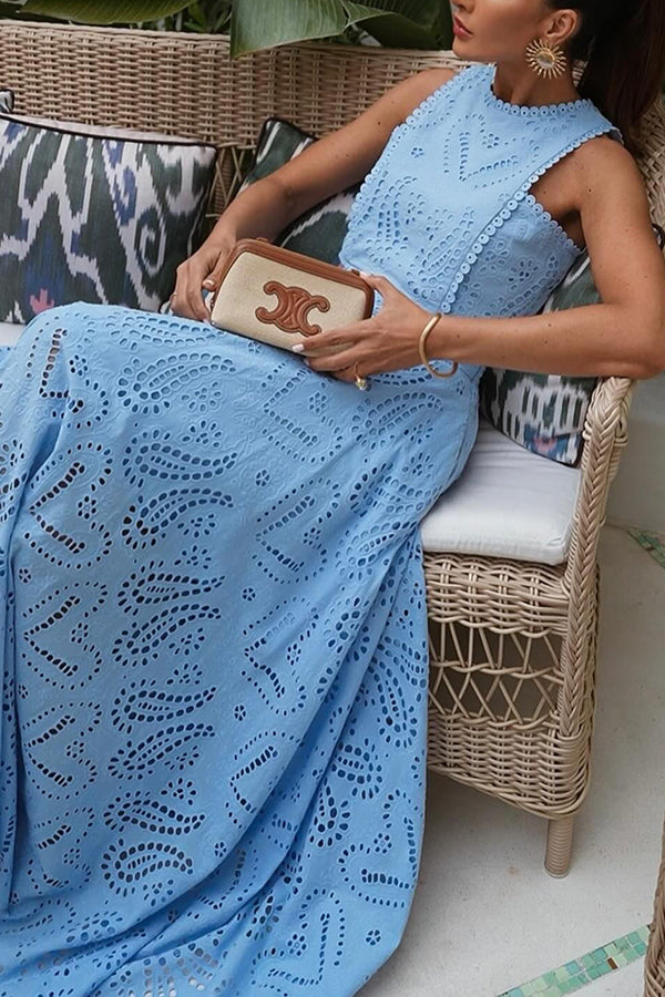 Model seated on a wicker couch in a blue embroidered top and skirt set holds a small clutch bag.