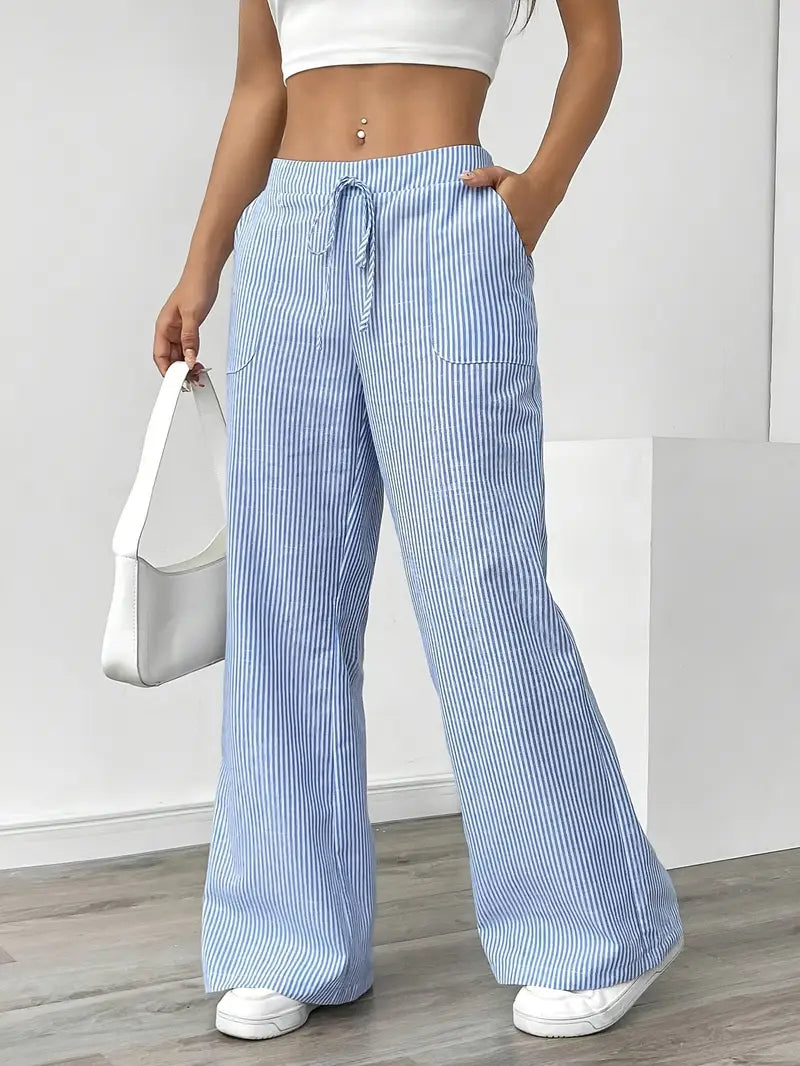 Blue and white striped relaxed pants with drawstring waist, displayed indoors, paired with white sneakers and bag.