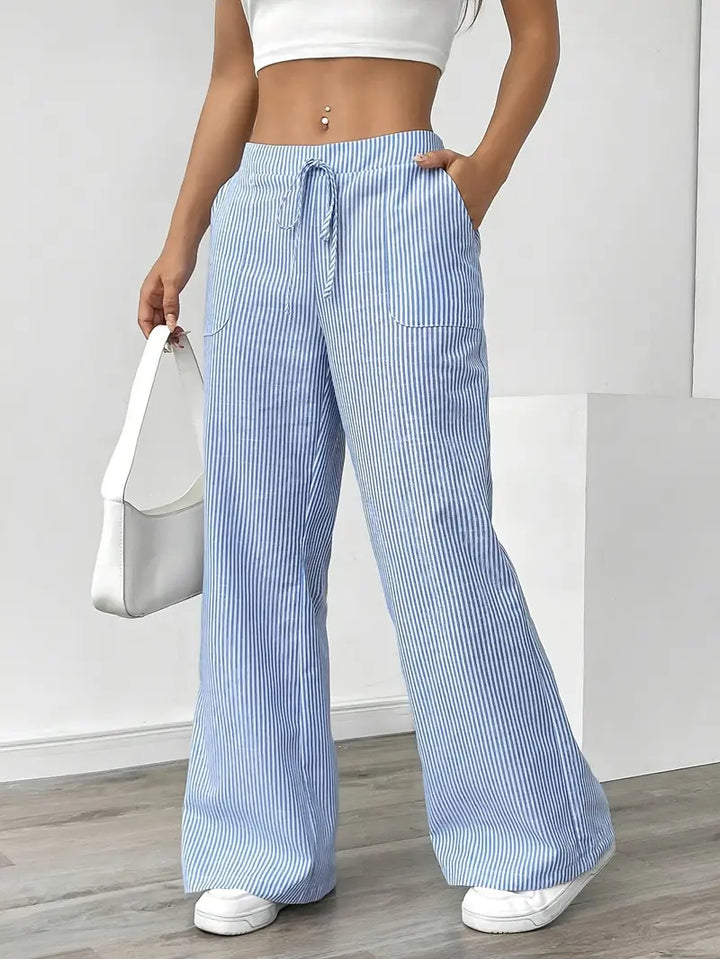 Blue and white striped relaxed pants with drawstring waist, displayed indoors, paired with white sneakers and bag.