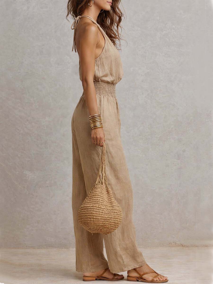 Side profile of beige jumpsuit with smocked high waist and halter neck, accessorized with bracelets. Studio setting.