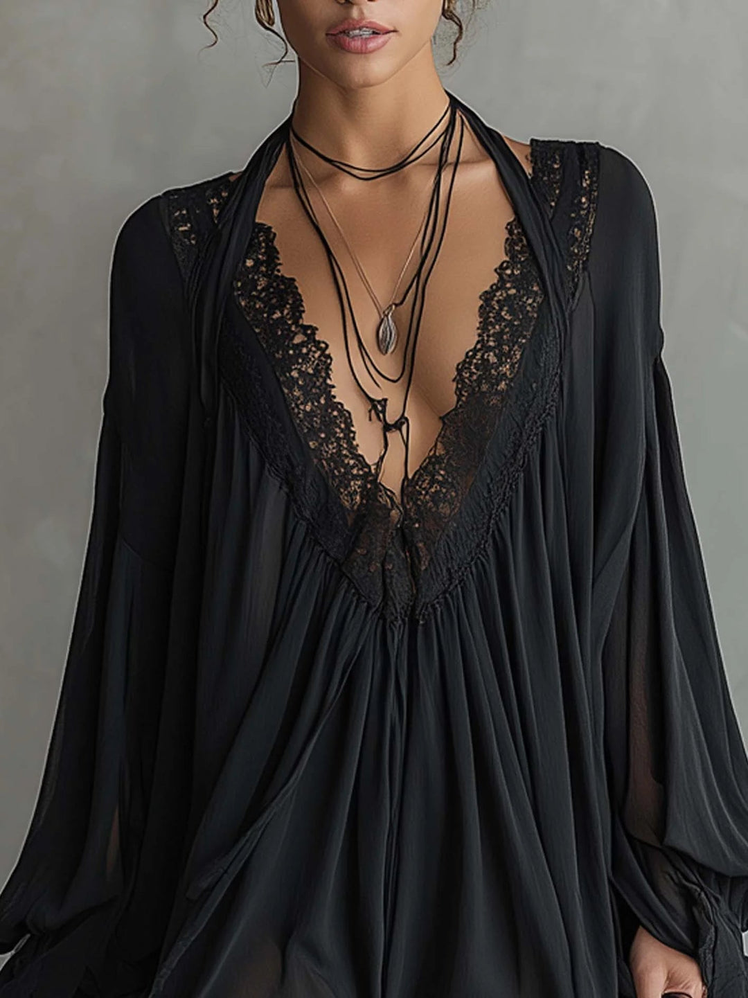 Front view of black mini dress with lace-trimmed neckline and layered necklaces, in a gray studio setting.