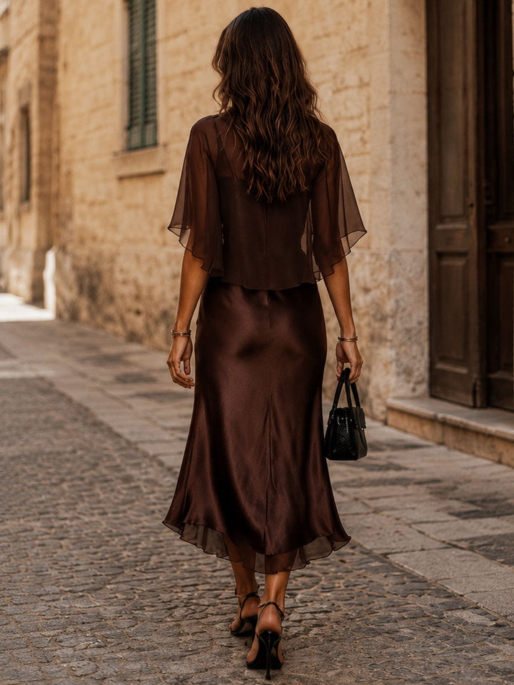 Back view of a brown midi dress with flowy overlay walking down a cobblestone street.
