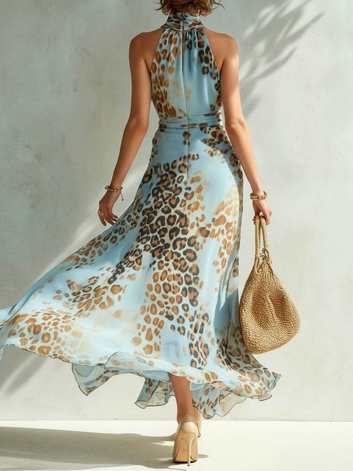 Back view of leopard print halter dress with flowing skirt, beige heels, straw bag. Light textured wall setting.