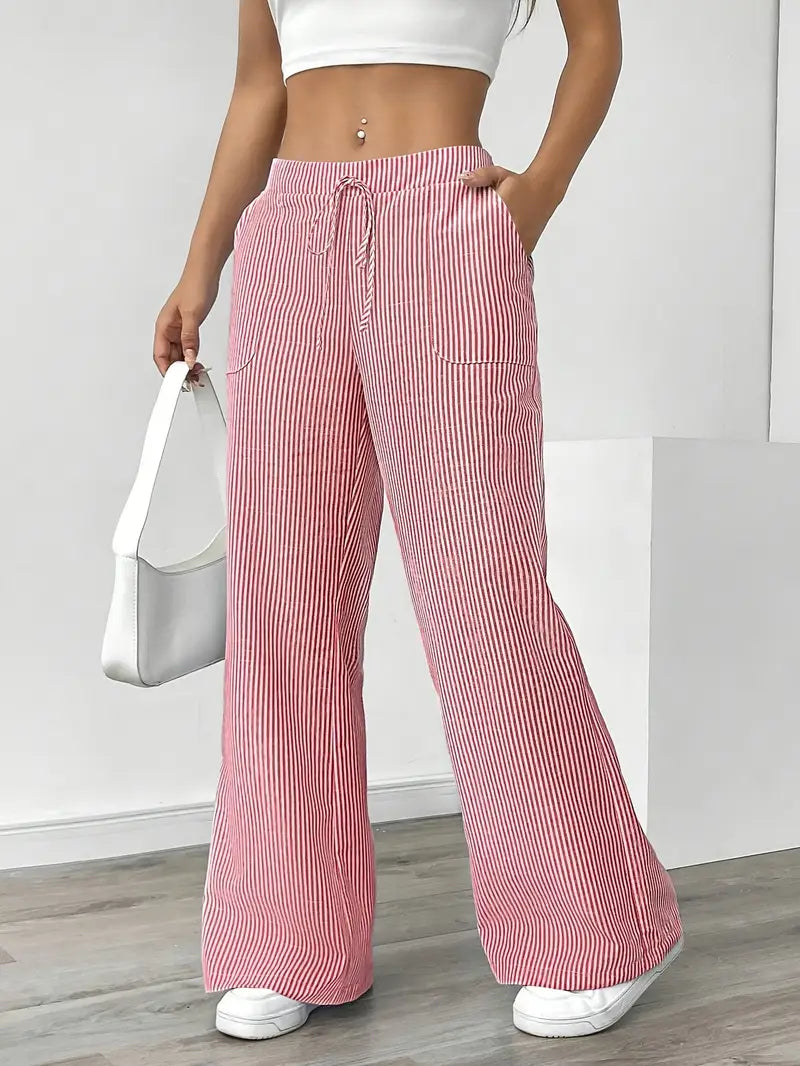 Red and white striped pants with pockets and drawstring, modeled indoors, paired with white sneakers and white bag.