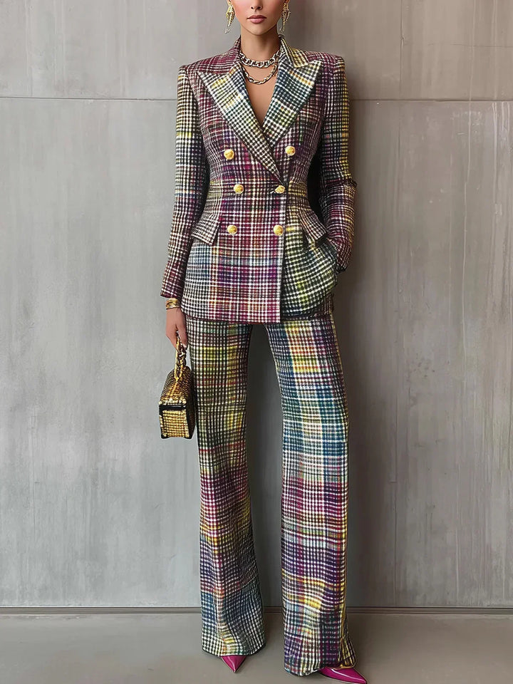Colorful plaid double-breasted suit with gold buttons, worn by a model holding a gold textured handbag, standing against a gray textured wall.