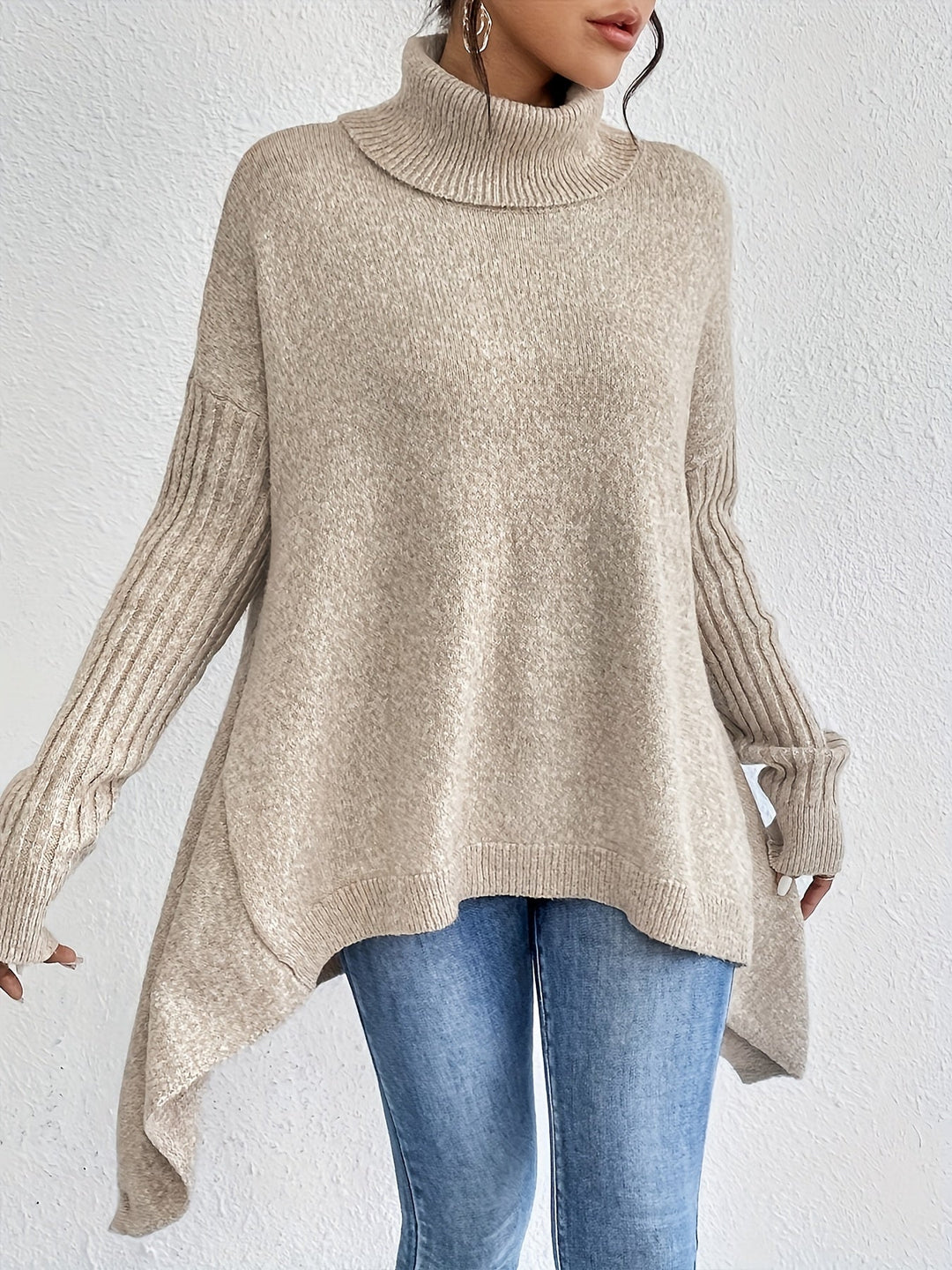 Beige turtleneck sweater with long sleeves, paired with jeans, positioned against a white wall.