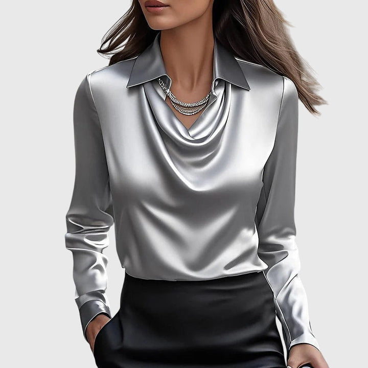 Shiny silver blouse with a draped neckline and long sleeves, paired with a black skirt, set against a simple background.