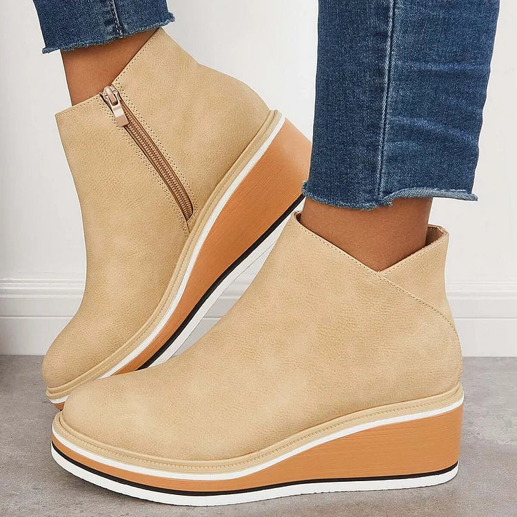 Beige luxe boots with wedge sole and zipper, paired with frayed jeans, on a gray floor and white wall.