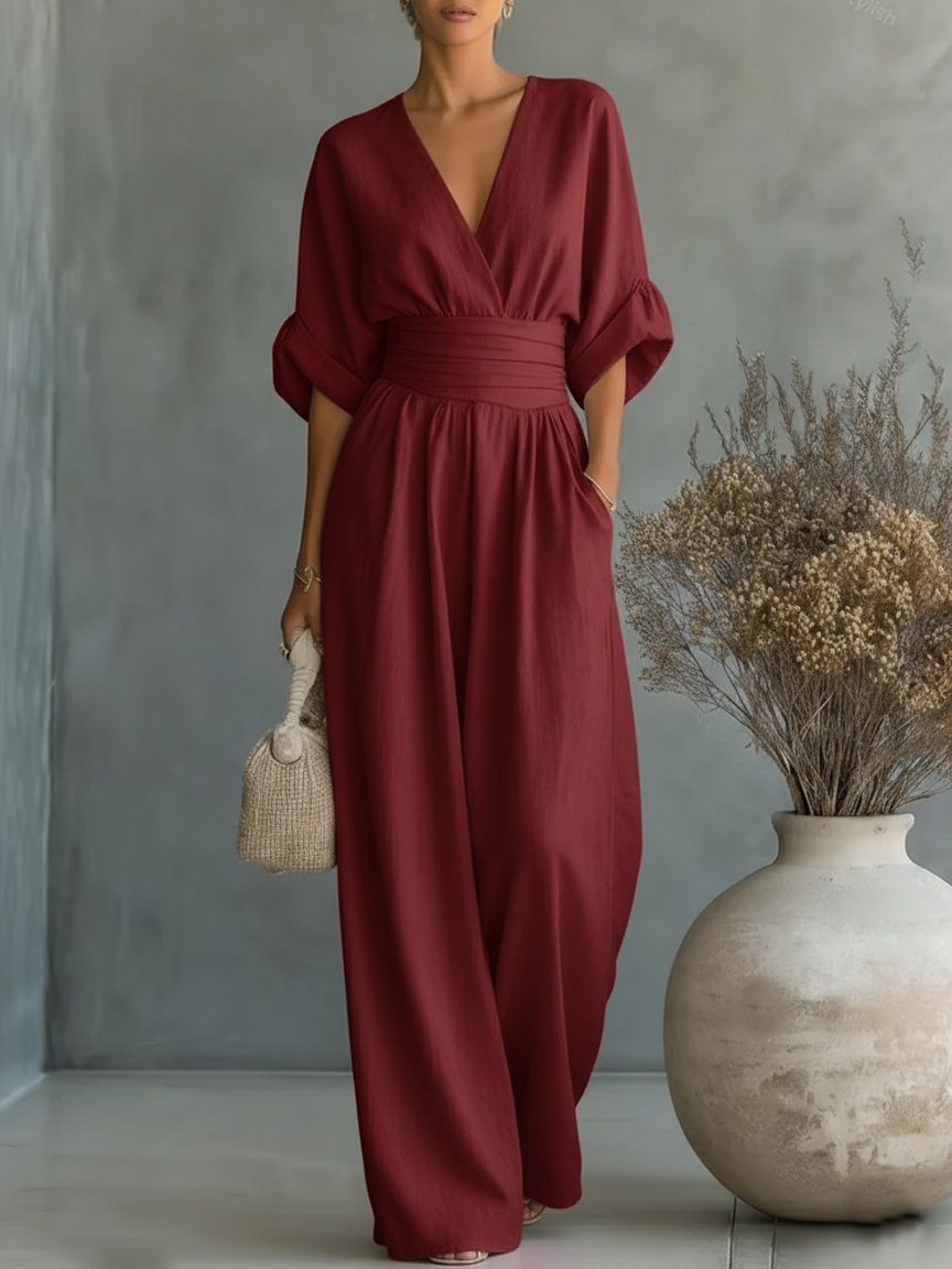 Burgundy V-neck high-waist jumpsuit with rolled-up sleeves, shown in a studio setting with a simple vase and dried foliage.