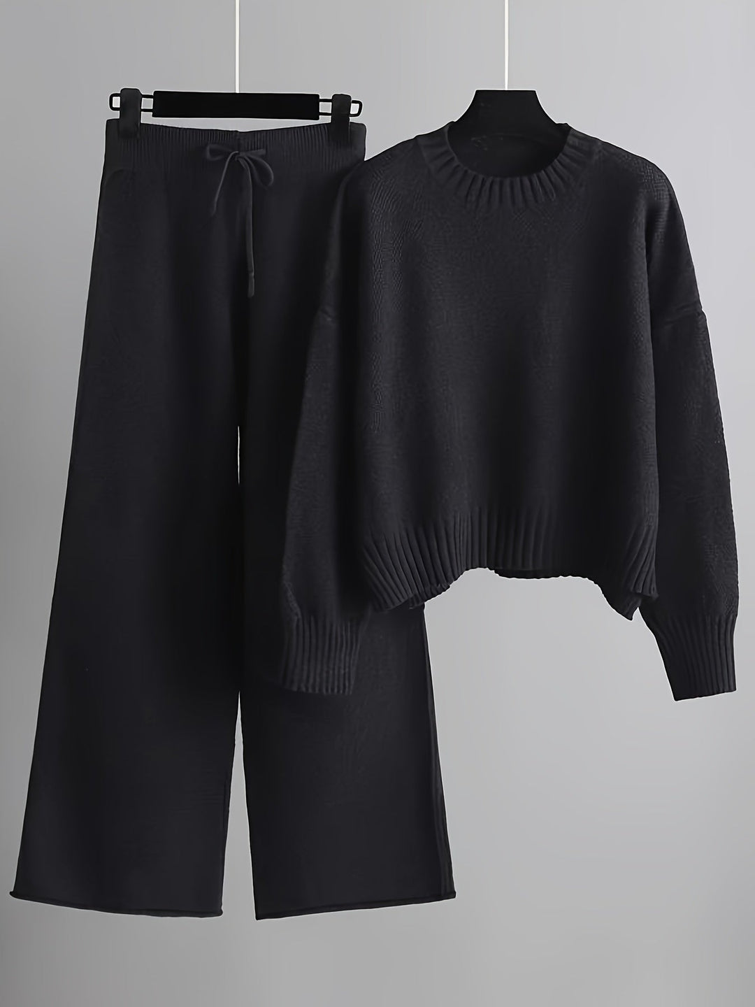 Dark gray knit loungewear set featuring a comfy sweater and wide-leg pants on hangers, gray background.