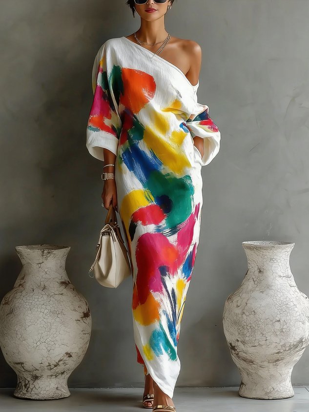 Colorful off-shoulder maxi dress with abstract design and vibrant splashes, paired with neutral sandals, in an indoor setting.