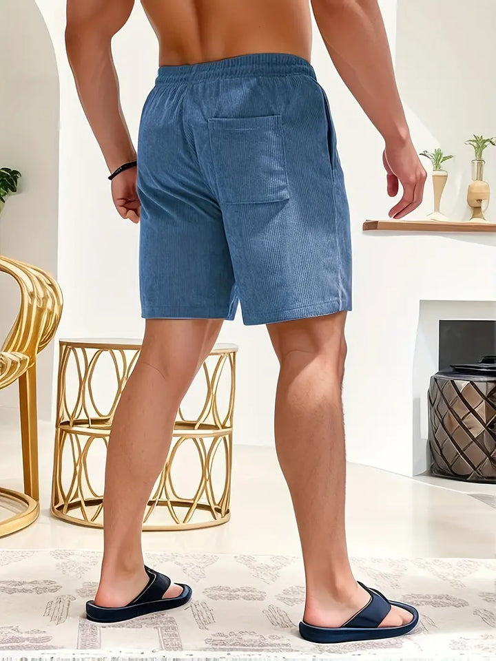 Back view of model in blue swimming trunks, standing indoors with decorative elements.