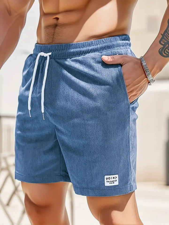 Close-up of blue swimming trunks with drawstring, worn by model outdoors in sunny setting.