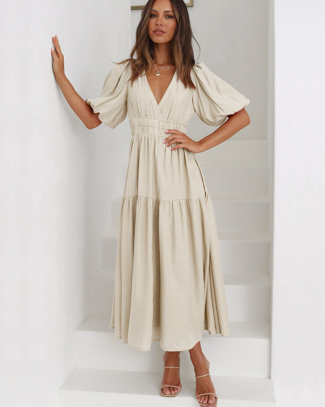 Woman in a cream midi dress with puff sleeves and V-neckline, standing on white stairs.