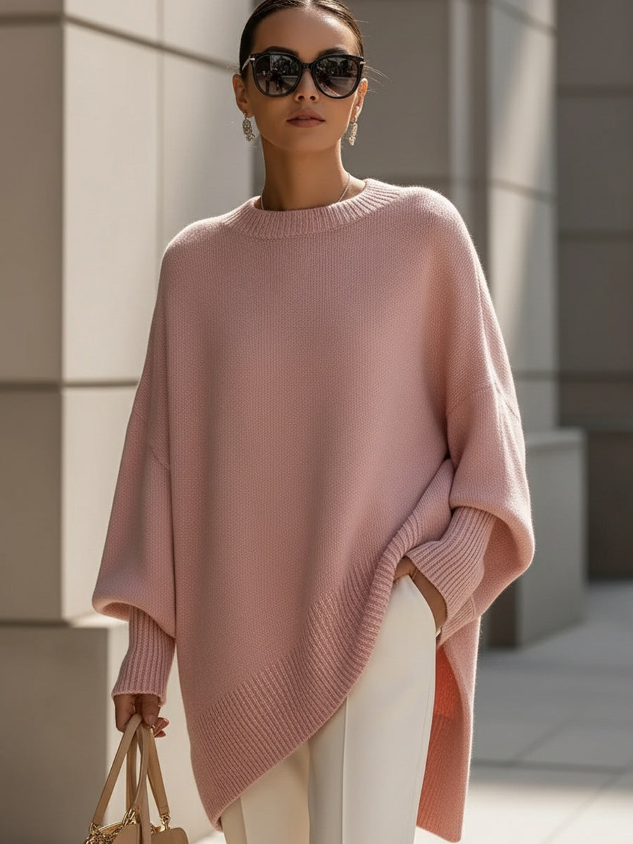 Woman in a loose pink sweater with ribbed hem and cuffs, wearing white pants, in an urban setting.