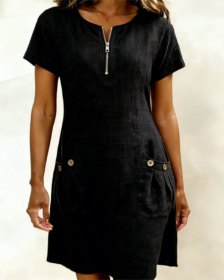 Black short-sleeve dress with zipper and buttoned pockets, studio background.