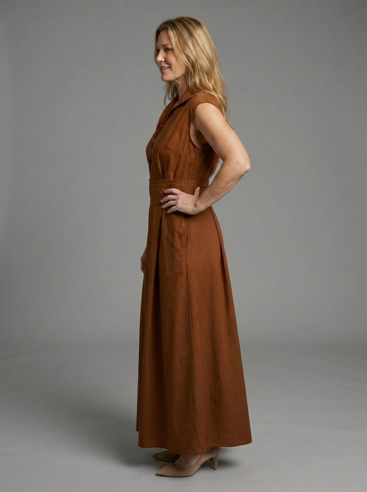 Side view of woman in brown sleeveless dress with wide waistband, posing in a studio with a gray background.