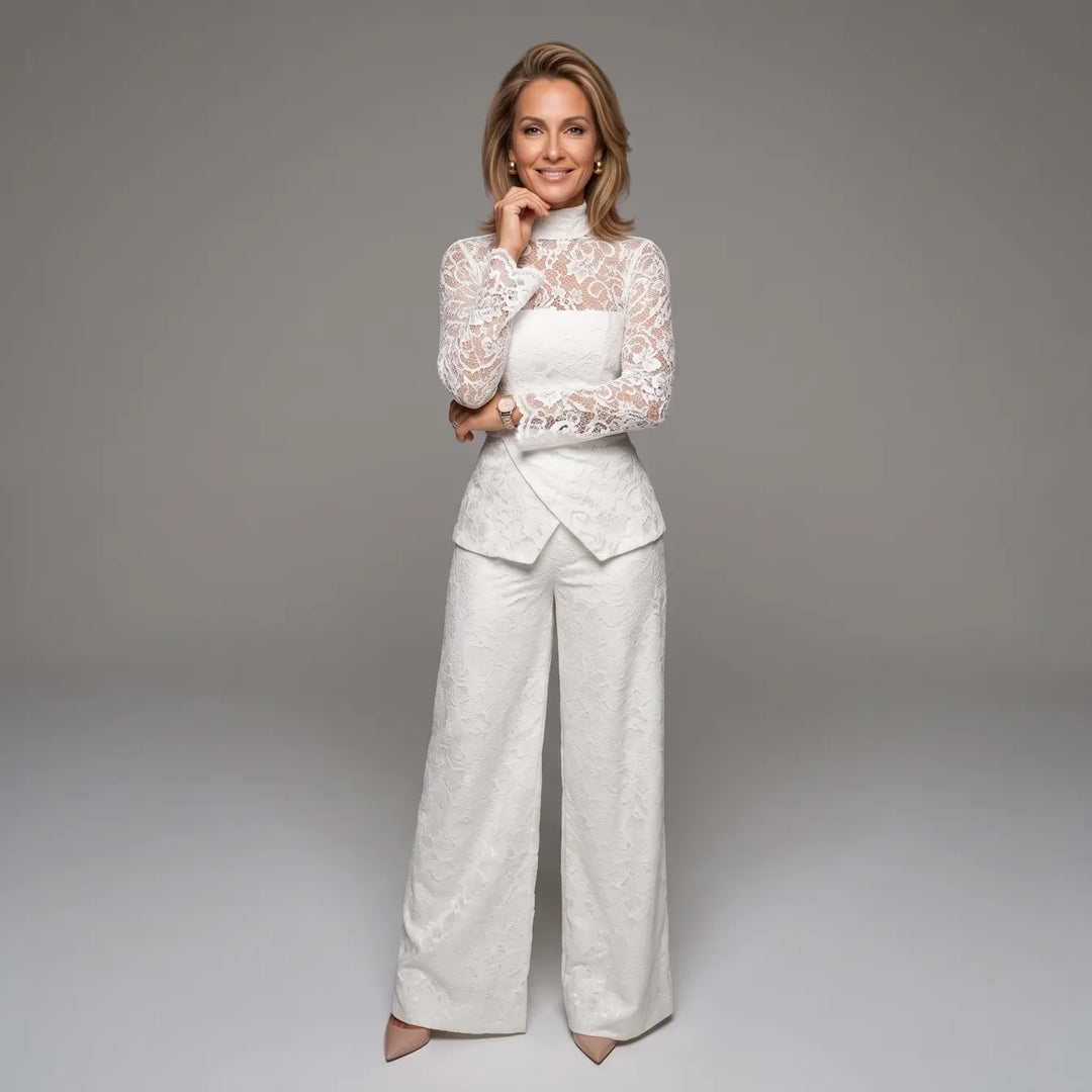 White lace jumpsuit with long sleeves, posed in a studio with gray background.