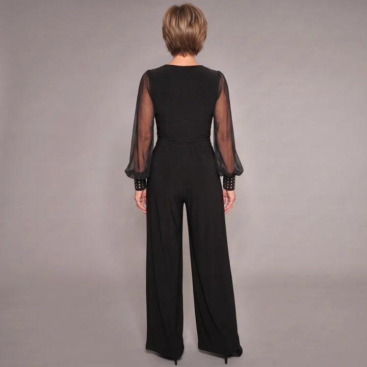 Back view of black jumpsuit showcasing sheer long sleeves and fitted waist, in a studio setting.