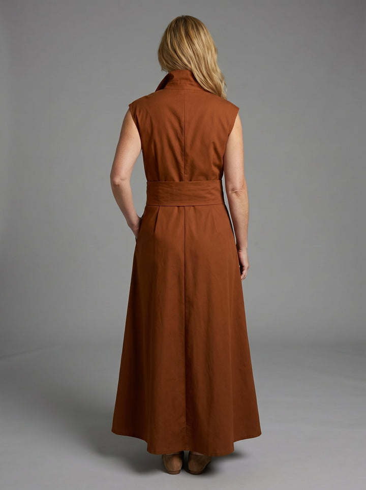 Back view of woman in brown sleeveless dress with wide waistband, posing in a studio with a gray background.