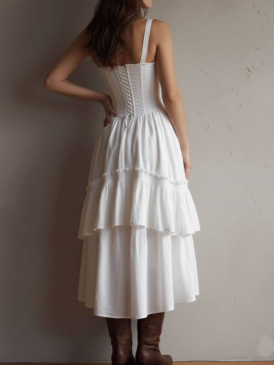 Back view of white tiered midi dress, fitted bodice, brown boots. Neutral textured background.