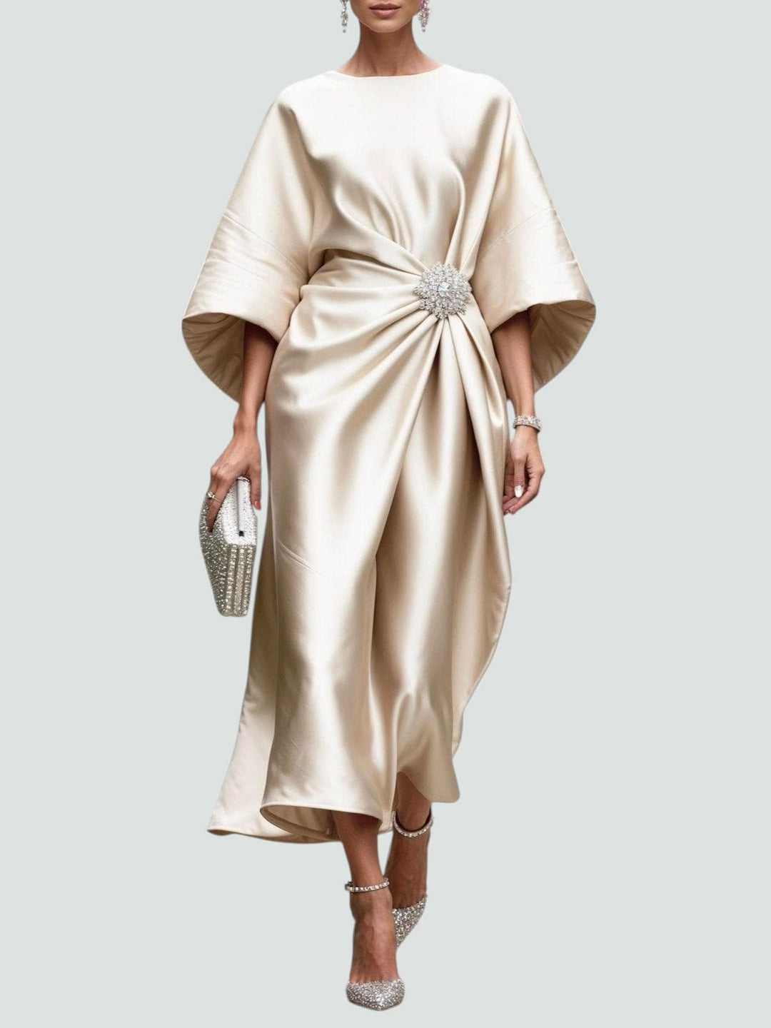 Elegant long satin dress in ivory with a floral brooch, paired with sparkly heels and a matching clutch, studio background.