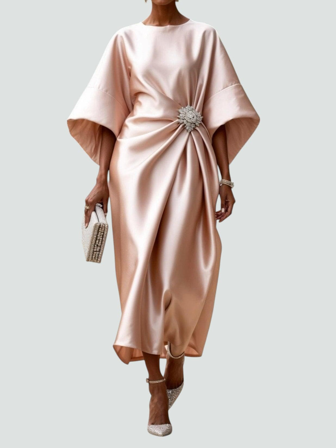 Elegant long satin dress in soft blush with a floral brooch, styled with sparkly heels and a matching clutch, studio background.