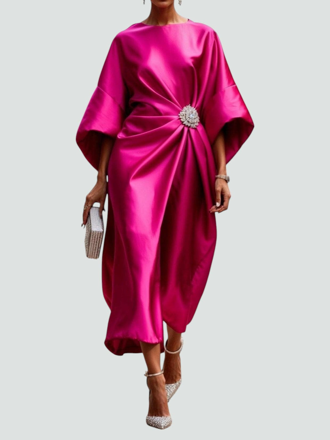 Elegant long satin dress in vibrant pink with a floral brooch, paired with sparkly heels and a matching clutch, studio background.