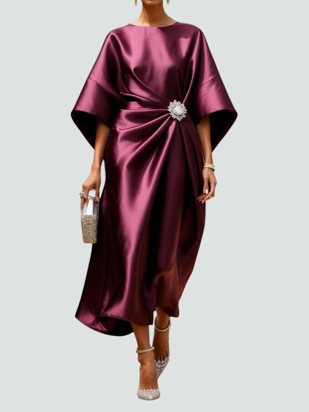 Elegant wine red dress with a decorative brooch, styled with sparkling heels and clutch against a light gray background.