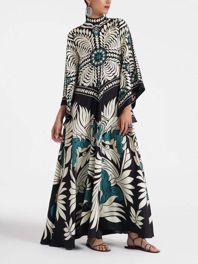 Flowy maxi dress with unique floral print in black, white, and teal, featuring a high neck and loose sleeves, modeled in studio.