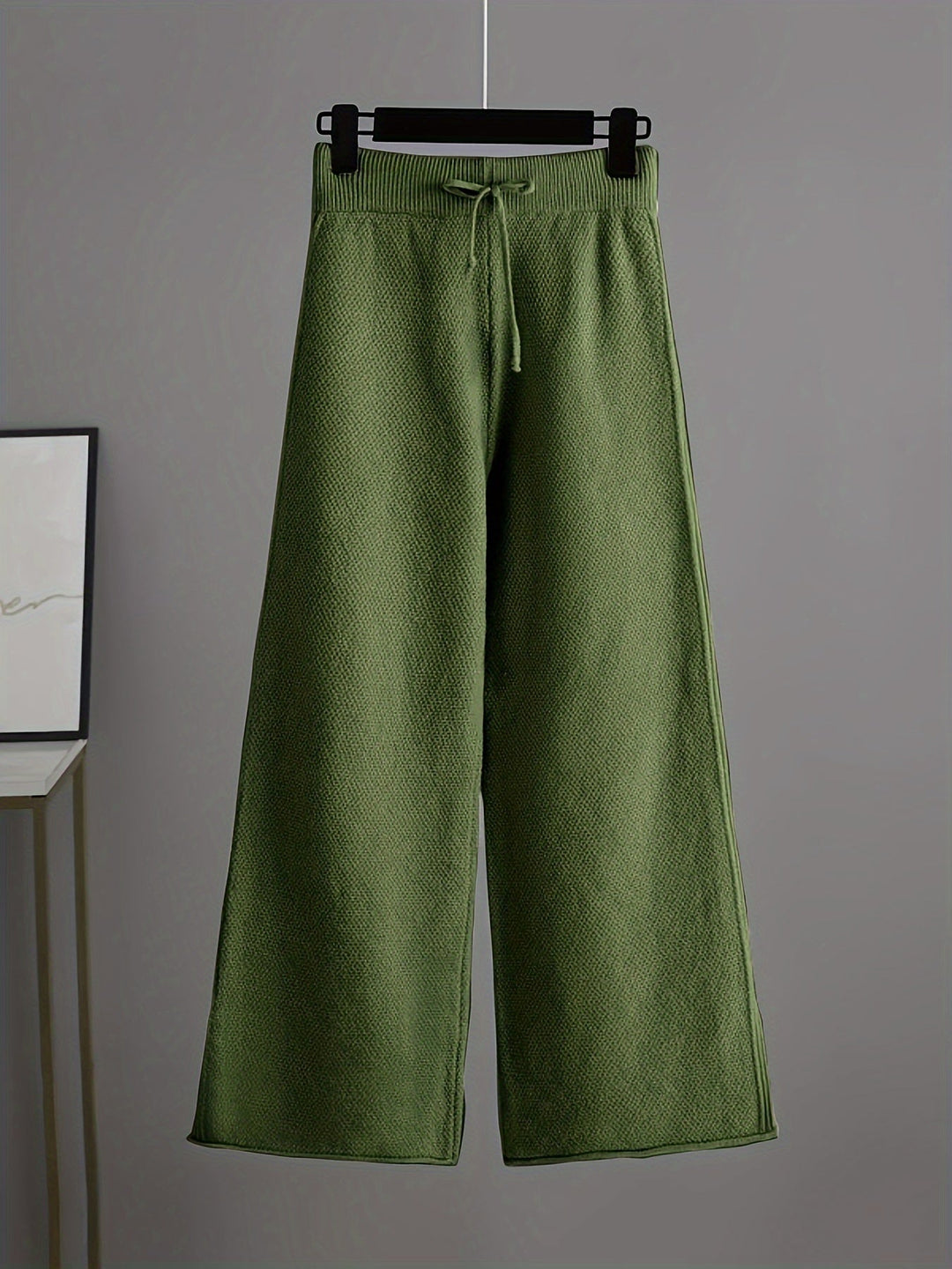 Olive green knit pants with a relaxed fit and drawstring on a hanger, gray background.