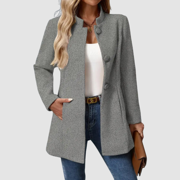 Gray jacket with large buttons, worn over white top and jeans, holding a clutch against a plain background.
