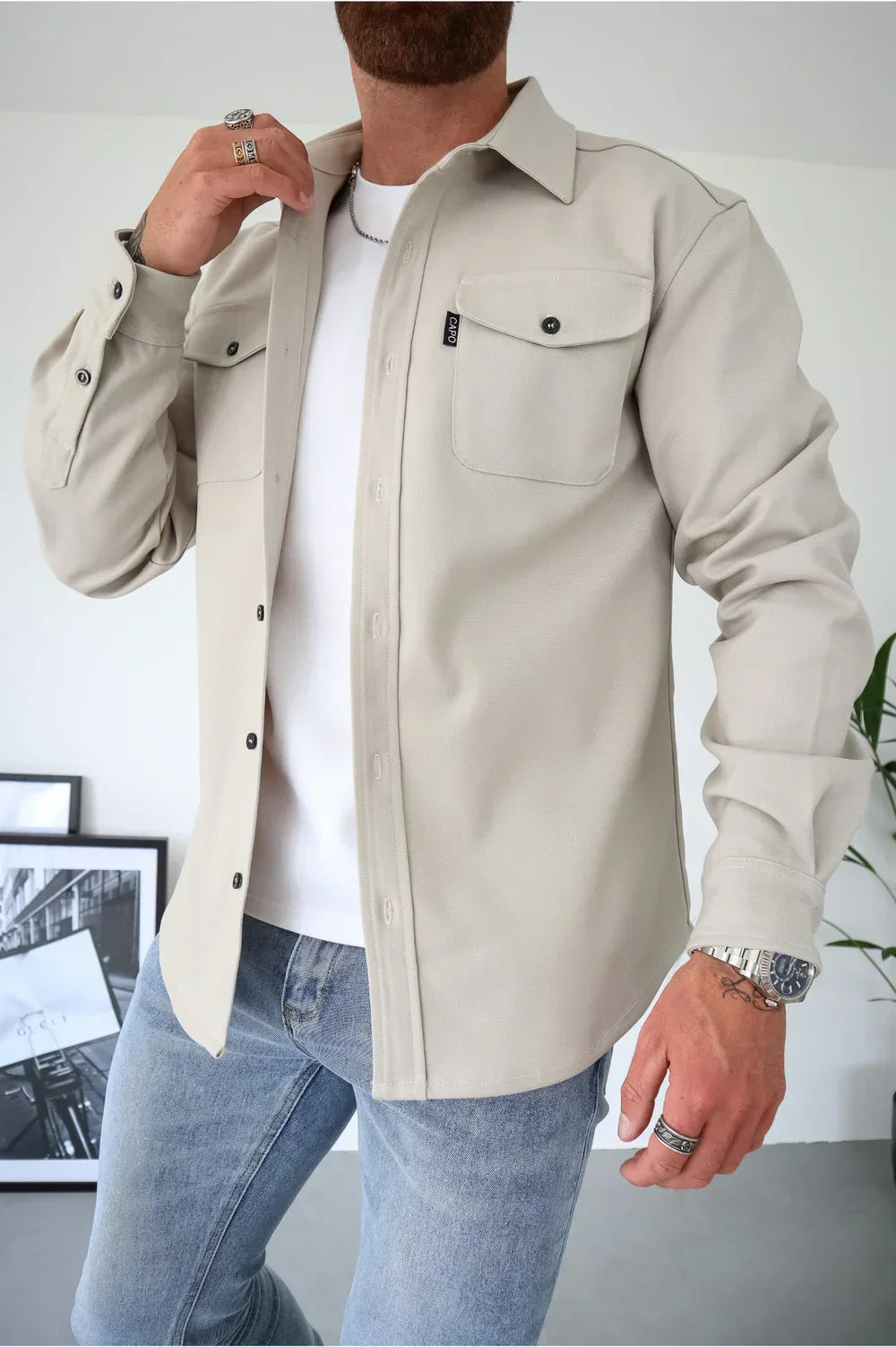 Light beige overshirt over white t-shirt and light jeans, person adjusting collar indoors.