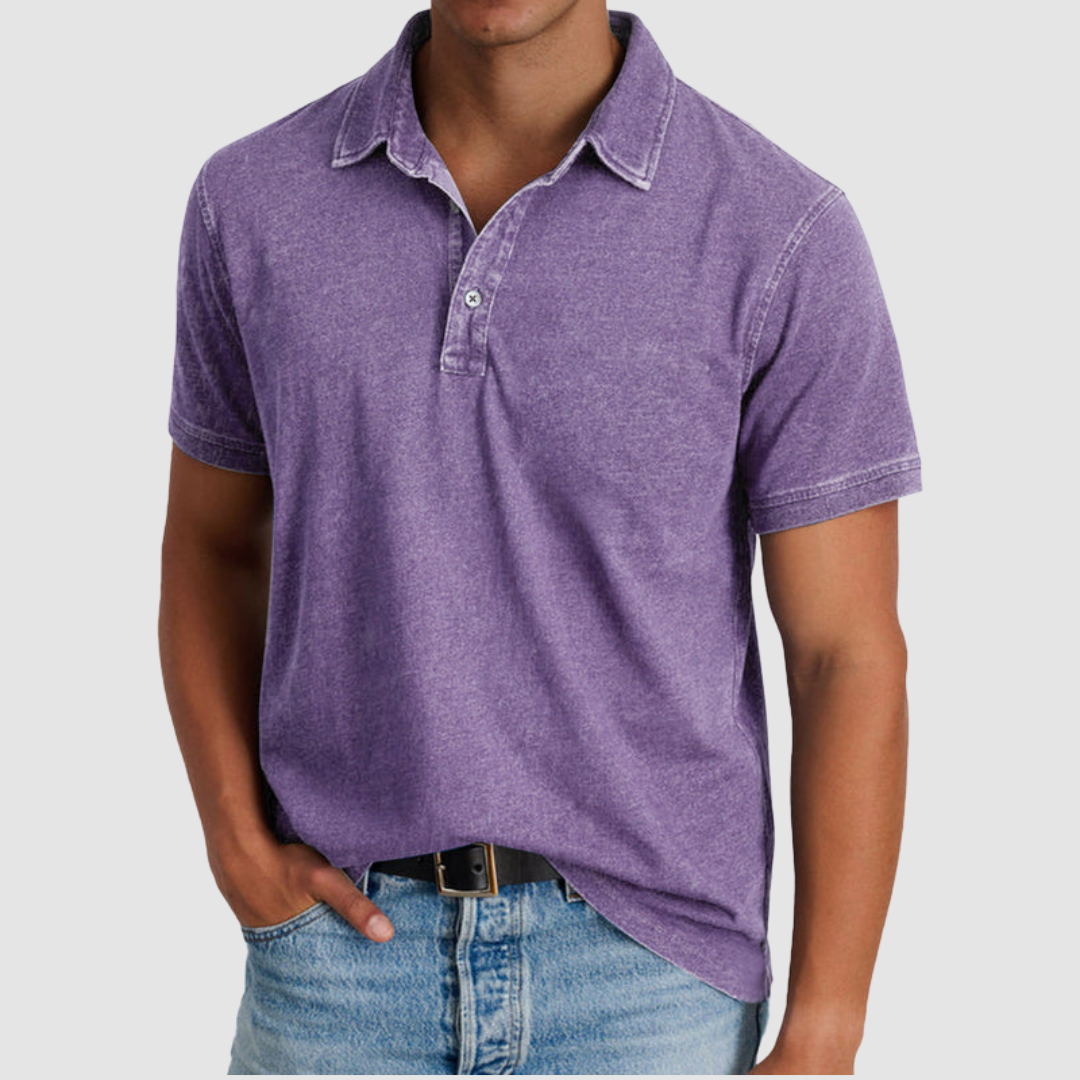 Man wearing a purple classic collared polo with short sleeves, buttoned placket, paired with jeans in a studio setting.